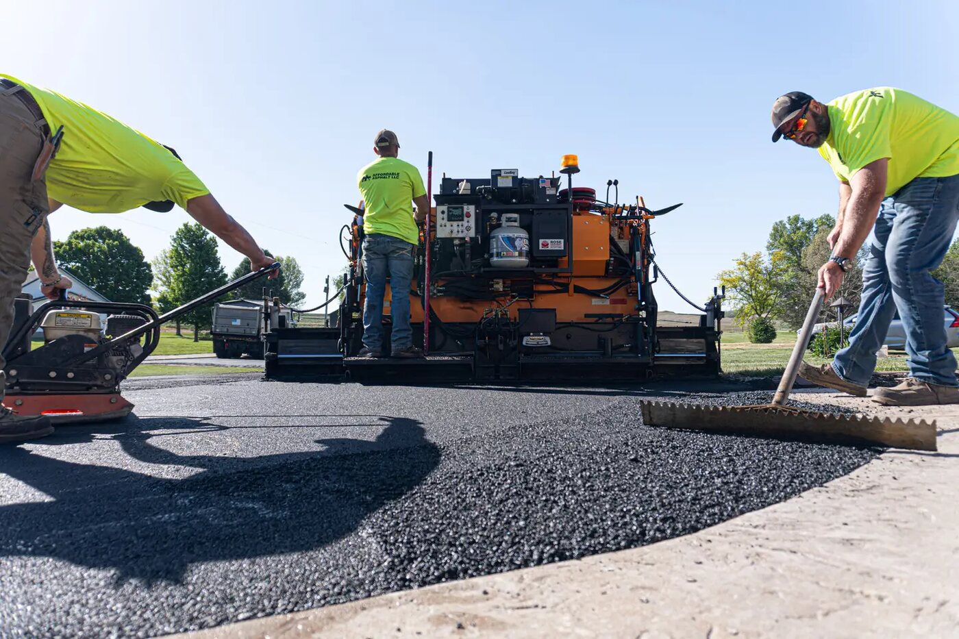 Paving crew hand-working fresh asphalt around a paver